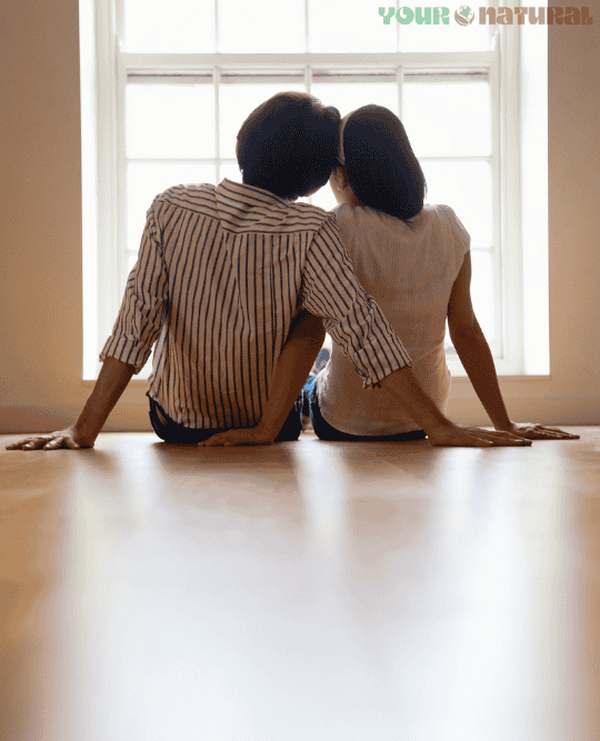 Couple sitting on the floor near a bright window, representing natural lifestyle choices and hormone health.